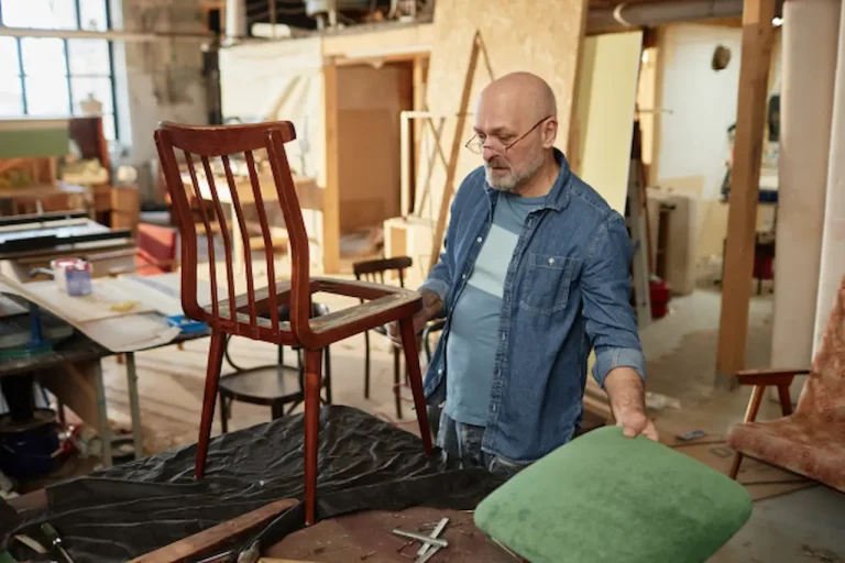 Un tapicero en el taller pensando sobre su nuevo trabajo. Podemos ver una silla para tapizar